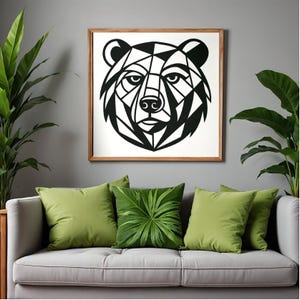 May include: A geometric black and white bear head art print in a wooden frame. The artwork hangs above a gray sofa with green throw pillows and leafy plants. The bear's face is composed of angular shapes.