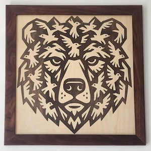 May include: Wooden wall art depicting a bear's face made of birds. The artwork is framed in a dark brown wooden frame. The bear's face is carved from light-coloured wood, with the birds and bear's features in a darker brown.