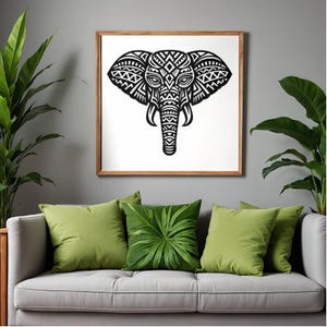May include: A framed monochrome elephant head artwork featuring detailed geometric designs. The picture hangs above a grey sofa with green cushions. Potted plants are positioned on either side of the sofa, enhancing the room's decor.