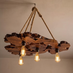 May include: A hanging chandelier featuring multiple natural wood slices arranged in a cluster. Four Edison-style light bulbs with visible filaments hang from the wood base, which is suspended by thick, braided jute rope attached to a ceiling mount.