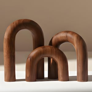 Op de afbeelding: Drie houten boogsculpturen in verschillende maten. De bogen zijn gemaakt van donkerbruin hout met zichtbare nerf. De sculpturen zijn samen gerangschikt, waardoor een visueel interessante weergave ontstaat. De gladde, gebogen vormen voegen een vleugje moderne elegantie toe.