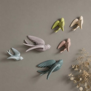 May include: A collection of six ceramic swallow wall ornaments in various pastel colors including light blue, lavender, pale green, cream, dusty pink, and dark teal, each depicted in a flying position with wings spread and tails fanned out.