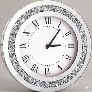 Könnte beinhalten: Eine runde Wanduhr mit weißem Zifferblatt, schwarzen römischen Ziffern und schwarzen Zeigern. Der Rahmen besteht aus einem verspiegelten Rand, der mit kleinen, reflektierenden silberfarbenen Kristallen besetzt ist und einen Glanzeffekt erzeugt.