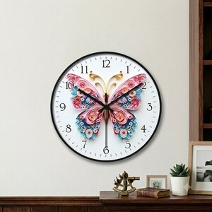 Peut inclure: Une horloge murale ronde avec un cadre noir et un cadran blanc comportant des chiffres noirs. Le centre de l'horloge présente un papillon détaillé réalisé en bandes de papier roulé dans des tons de rose, bleu et or, avec des aiguilles noires.
