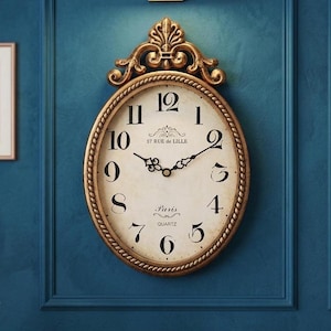 May include: An oval-shaped wall clock with a gold-colored frame and a cream-colored face. The clock features black Roman numerals, black hands, and the text "57 RUE de LILLE" and "Paris QUARTZ". The clock is mounted on a blue wall.