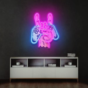 May include: A neon sign featuring a hand making a rock and roll gesture while holding a video game controller. The sign glows with vibrant pink and blue light, showcasing a detailed outline of the hand and the controller buttons in a bright display.