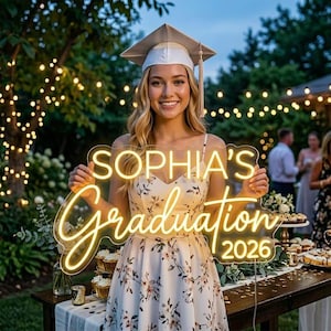 May include: A young woman in a graduation cap and floral dress holds a glowing neon sign that reads "SOPHIA'S Graduation 2026". The sign is illuminated with a warm, yellow light. The background includes string lights and a table with desserts.