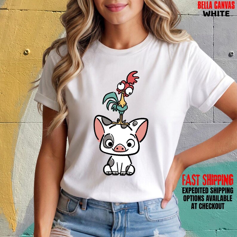 May include: White Bella Canvas t-shirt featuring a cartoon illustration of a pig with a rooster on top. The pig is white with black spots and pink ears. The rooster is red, green, and yellow. The shirt also has the text "FAST SHIPPING".