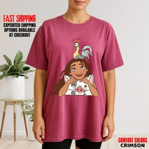 May include: Crimson Comfort Colors t-shirt with a cartoon illustration of a girl, a pig, and a rooster. The girl has brown hair and is smiling. The pig is white with black spots. The rooster is yellow and grey.