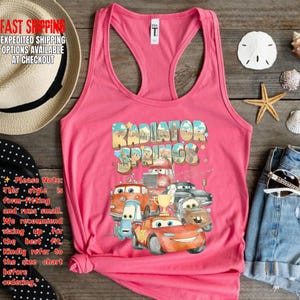 Puede incluir: Camiseta sin mangas rosa con un gr&aacute;fico colorido de personajes de la pel&iacute;cula "Cars" con el texto "Radiator Springs". La camiseta sin mangas tiene cuello redondo y dise&ntilde;o de espalda deportiva.