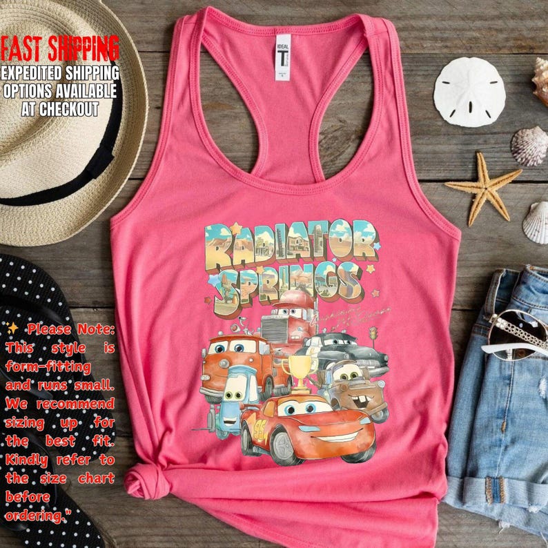 Puede incluir: Camiseta sin mangas rosa con un gr&aacute;fico colorido de personajes de la pel&iacute;cula "Cars" con el texto "Radiator Springs". La camiseta sin mangas tiene cuello redondo y dise&ntilde;o de espalda deportiva.