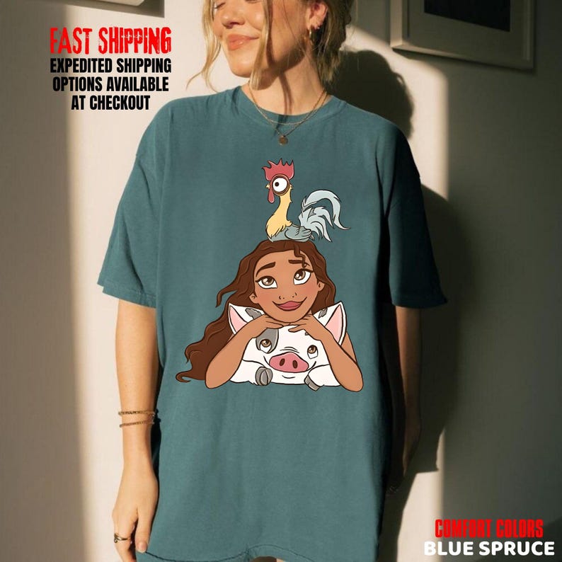 May include: Blue spruce t-shirt with a cartoon graphic of a woman, a pig, and a rooster. The shirt has the text "COMFORT COLORS" and "BLUE SPRUCE".