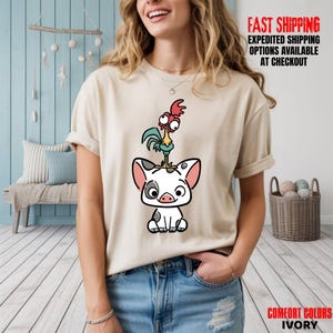 May include: Ivory-colored t-shirt featuring a cartoon illustration of a pig with a rooster on its head. The pig is white with black spots and pink ears. The rooster is red, green, and yellow. Text on the shirt reads "FAST SHIPPING" and "COMFORT COLORS IVORY".