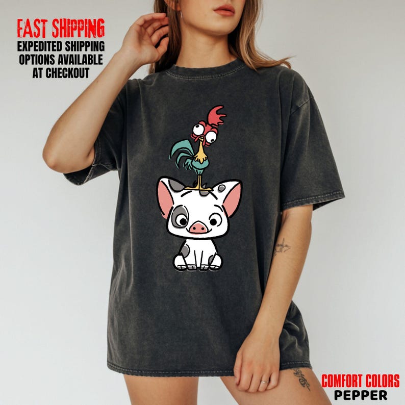 May include: Dark gray t-shirt featuring a cartoon illustration of a pig with a rooster on its head. The pig is white with black spots and pink ears. The rooster is blue, red, and yellow. The shirt also has the text "COMFORT COLORS PEPPER".