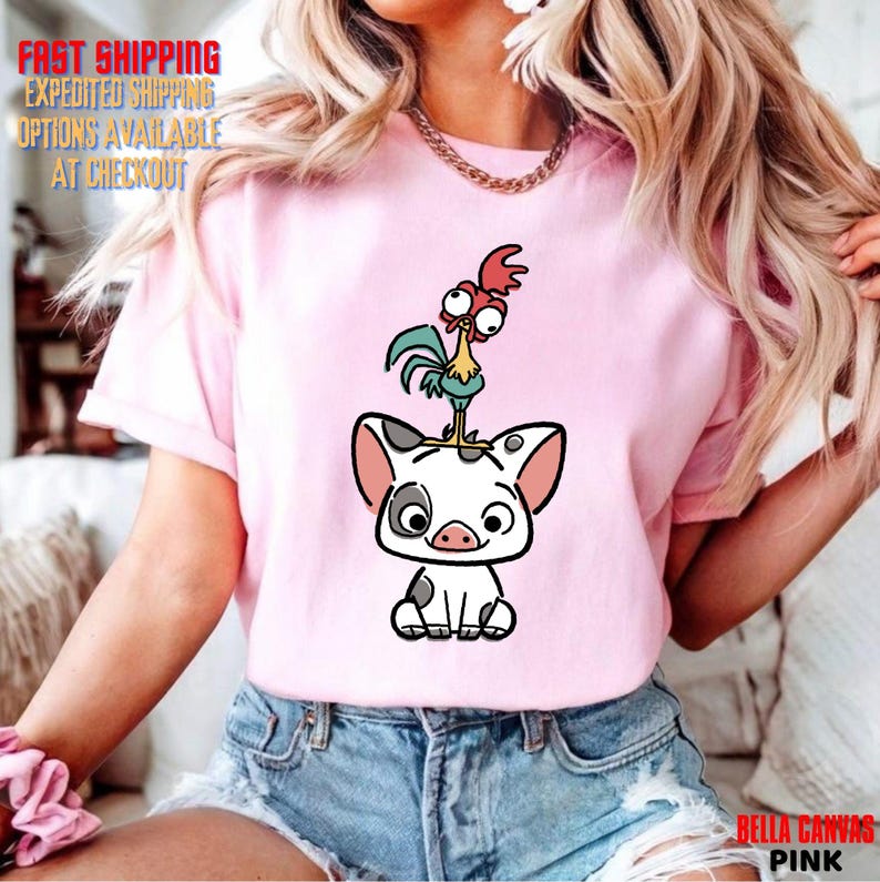 May include: Pink t-shirt featuring a cartoon illustration of a pig with a rooster on top. The pig is white with black spots and a pink nose. The rooster is red, green, and blue. The shirt also has the text "BELLA CANVAS PINK".