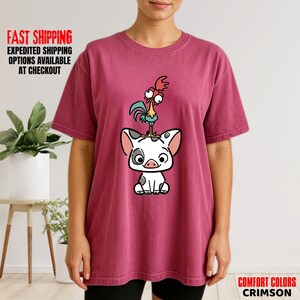 May include: Crimson Comfort Colors t-shirt featuring a cartoon illustration of a pig with a rooster on its head. The pig is white with black spots and the rooster is yellow, red, and blue. The shirt has the text "Comfort Colors Crimson".