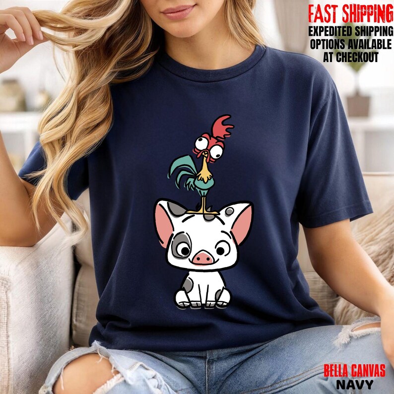 May include: Navy blue t-shirt featuring a cartoon illustration of a pig with a rooster on top. The pig is white with black spots and the rooster has red, yellow, and blue accents. The text "BELLA CANVAS NAVY" is at the bottom.
