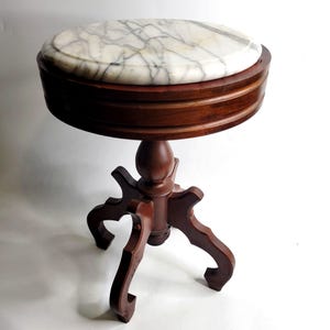May include: A round side table featuring a white marble top with grey veining. The table has a dark brown wooden frame with a thick circular apron and a central pedestal base supported by three curved legs that extend outward from the center.