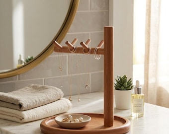 May include: A wooden jewelry organizer with a round base and a vertical post with pegs for hanging necklaces and earrings. A small dish holds rings and other jewelry. The organizer is on a marble countertop.