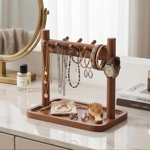 May include: A wooden jewelry organizer with a tray base and vertical posts. Various necklaces, bracelets, earrings, and a watch are displayed. A small bag, rings, and a brush are also on the tray. The organizer is on a white surface.