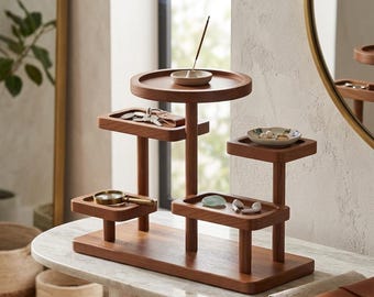 May include: A multi-tiered wooden organizer with various trays and platforms. The organizer holds keys, a magnifying glass, jewelry, and other small items. An incense stick burns on the top tier. The organizer is made of a warm-toned wood.