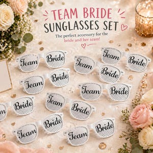 May include: A set of white sunglasses with the words "Team Bride" printed on them. The sunglasses are arranged on a table with flowers and a sign that says "Bride Tribe". The image is well-lit and features a romantic theme.