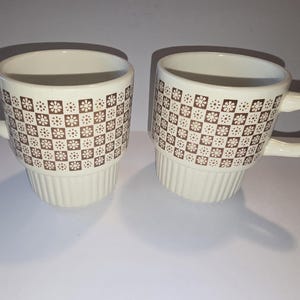 May include: A white ceramic mug with a black handle and the text "But First, Coffee" in a bold, black font. The mug is set against a blurred background, suggesting a cozy setting. The mug appears to be approximately 4 inches tall.