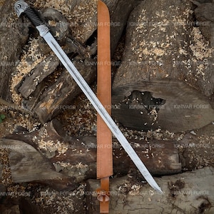 May include: A long, silver sword with an eagle head handle and a black grip, lying on wood. The sword has a brown leather sheath. The blade is etched with a pattern. The sheath is brown.