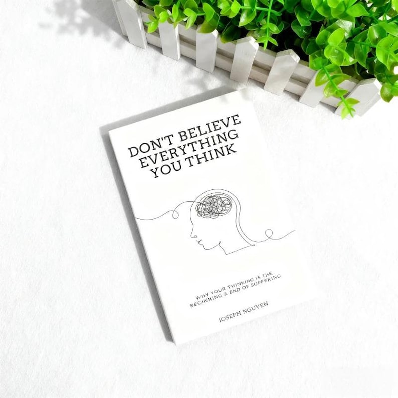 Może przedstawiać: Biała książka zatytułowana "DON'T BELIEVE EVERYTHING YOU THINK" z minimalistyczną ilustracją głowy i m&oacute;zgu. Książka zawiera r&oacute;wnież tekst "WHY YOUR THINKING IS THE BEGINNING & END OF SUFFERING" oraz nazwisko autora, JOSEPH NGUYEN.
