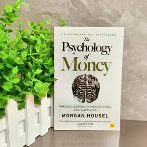 Może przedstawiać: Książka w twardej oprawie zatytułowana "The Psychology of Money" ze złotą i białą okładką. Okładka zawiera tytuł, autora Morgana Housel i ilustrację m&oacute;zgu. Książka jest bestsellerem o bogactwie, chciwości i szczęściu.