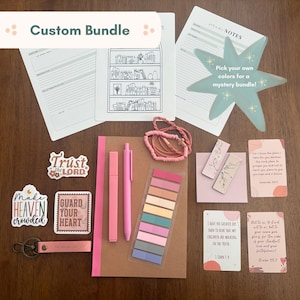 May include: A custom bundle of stationery items in shades of pink and neutral tones. Includes stickers, pens, sticky notes, a journal, and cards with inspirational quotes. The bundle is designed for journaling and note-taking.