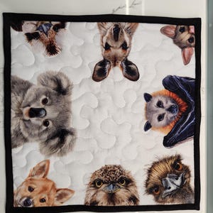May include: Square quilted fabric with a white background and a black border, patterned with Australian animals. The design includes a koala, kangaroo, bat, and owl, arranged in a repeating pattern across the fabric.