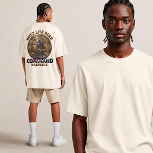 Può includere: T-shirt bianco sporco con grafica sul retro con la scritta "BUZZ LITE BEER PREMIUM CRAFT ASTRONAUT" e "STAR COMMAND BREWERY". La t-shirt è abbinata a pantaloncini color cachi e scarpe da ginnastica bianche. La t-shirt è indossata da un modello.