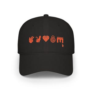 Op de afbeelding: Een zwarte honkbalpet met een reeks oranje grafische iconen op de voorkant. De iconen bestaan uit een handgebaar, een silhouet van een kat, een basketbalhart, een hangslot met een cirkelvormig embleem en een boog met een klein figuurtje.