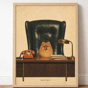 Pode incluir: Uma impressão emoldurada com um Pomerânia laranja fofo sentado numa cadeira de escritório de couro verde-escuro atrás de uma secretária de madeira. Na secretária estão um telefone de disco laranja vintage, uma pilha de papéis e um candeeiro de latão. O texto diz HOLD MY CALLS.