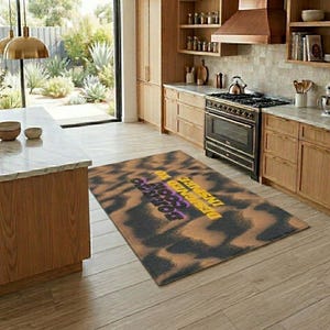 Könnte beinhalten: Ein rechteckiger Teppich mit einem Batikmuster in Braun- und Schwarztönen. Der Teppich trägt den Text "DESIGNED TO INSPIRE GOOD VIBES" in Lila und Gelb. Der Teppich liegt auf einem Holzboden in einer Küche.