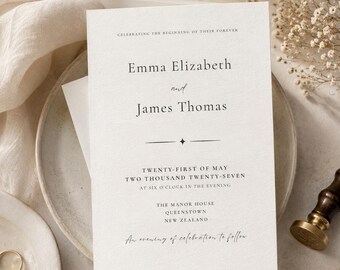 May include: A white wedding invitation card with black serif and script text reading Emma Elizabeth and James Thomas, Twenty-First of May Two Thousand Twenty-Seven, The Manor House, Queenstown, New Zealand, and An evening of celebration to follow.