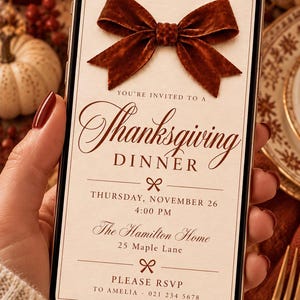 May include: A smartphone displaying a digital Thanksgiving dinner invitation featuring a dark brown velvet bow at the top. The text reads: You're invited to a Thanksgiving Dinner, Thursday, November 26, 4:00 PM, The Hamilton Home, 25 Maple Lane, Please RSVP to Amelia - 021 234 5678.