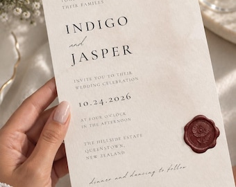 May include: A cream-colored wedding invitation card featuring black serif and script typography. The text reads: Together with their families, Indigo and Jasper, invite you to their wedding celebration, 10.24.2026, at four o'clock, The Hillside Estate, Queenstown, New Zealand, dinner and dancing to follow. A dark red wax seal with a floral design is attached to the bottom right corner.