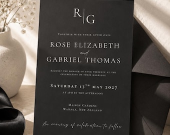 May include: A rectangular black wedding invitation card featuring white serif and script typography. The text includes the initials RG, the names Rose Elizabeth and Gabriel Thomas, the date Saturday 13th May 2027, and the location Maison Gardens, Wanaka, New Zealand.