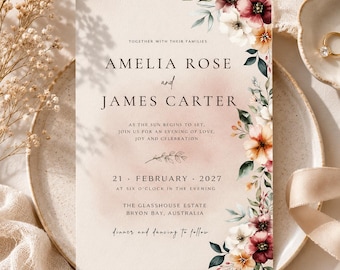 May include: A wedding invitation card featuring a soft blush background with a floral arrangement of deep red, white, and orange flowers along the right side. The text reads Amelia Rose and James Carter, 21 February 2027, at The Glasshouse Estate.
