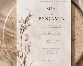 May include: A rectangular wedding invitation card featuring a watercolor illustration of dried wildflowers on the left side. The text reads: TOGETHER WITH THEIR FAMILIES, MIA and BENJAMIN, INVITE YOU TO THEIR WEDDING CELEBRATION, 06.03.2027, AT FOUR O'CLOCK IN THE AFTERNOON, THE HILLSIDE ESTATE, QUEENSTOWN, NEW ZEALAND, celebration to follow.