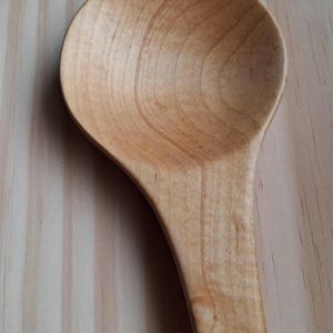May include: A wooden spoon with a rounded bowl and a long handle. The spoon is made of light-colored wood, with visible grain patterns. The spoon is likely used for cooking or serving food.