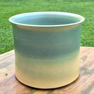 Peut inclure: Un pot de fleurs cylindrique en céramique présentant une finition dégradée lisse qui passe d'un jaune pâle doux à la base à un vert sauge atténué au niveau du bord supérieur. Le récipient a une large ouverture et une silhouette simple et épurée.
