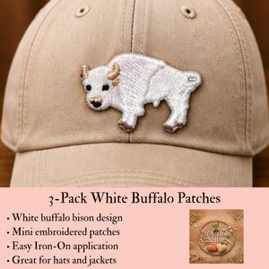 May include: A tan baseball cap featuring a white embroidered buffalo patch on the front. The patch depicts a white bison with tan-colored horns and hooves. The cap has a structured crown with stitched eyelets and a curved brim.