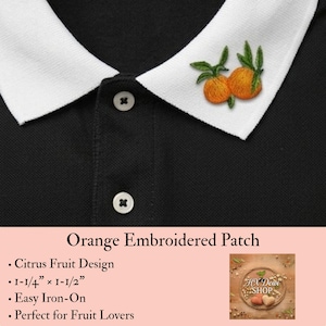 May include: A black polo shirt with a white collar featuring an embroidered patch of two orange citrus fruits with green leaves. The patch measures 1-1/4 inches by 1-1/2 inches. The shirt has two white buttons on the front placket.