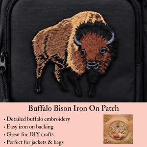 May include: A black fabric surface featuring an embroidered patch of a brown and black buffalo bison. The patch displays detailed stitching of the animal's fur, horns, and facial features. Below the patch, text reads Buffalo Bison Iron On Patch.