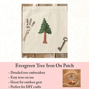 May include: A cream-colored tote bag with a detailed green and brown embroidered evergreen tree patch. The bag also features a sprig of lavender and a vintage key. The text on the image says "Evergreen Tree Iron On Patch".