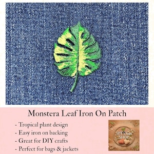 May include: An embroidered monstera leaf patch featuring variegated shades of dark green, light green, and yellow, stitched onto a dark blue denim fabric background. The patch has a distinct split-leaf design with a central stem and textured thread.
