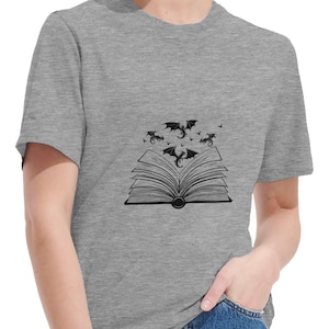 Könnte beinhalten: Ein meliertes graues T-Shirt mit einer schwarzen Illustration eines offenen Buches, aus dem Drachen und Fledermäuse fliegen. Das T-Shirt besteht aus weichem Material und hat einen klassischen Rundhalsausschnitt.